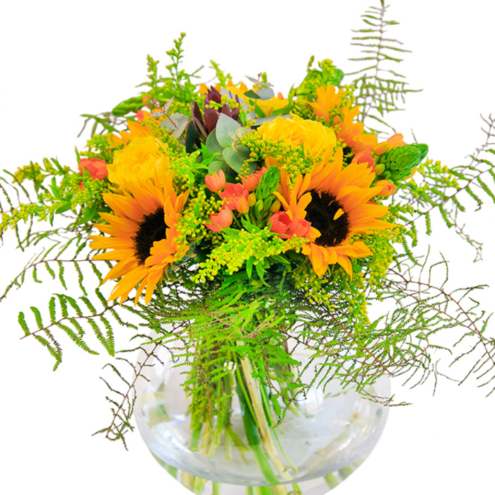 From the first glance, this abundant arrangement echoes the sunlit optimism of St Mary Cray's summer festivals, its colors and textures captivating and lively. Towering sunflowers with robust brown cores and glowing yellow petals anchor the bouquet, evoking bright afternoons spent near the High Street or in riverside parks. Tucked amongst them, yellow garden roses, each bloom delicately spiralling outwards, provide a sense of gentle refinement and enduring beauty. Pops of scarlet hypericum berries gleam amidst the foliage, their presence both whimsical and striking. Feathery green ferns spill downward from the bouquet's edge, reminiscent of the wild flora along the waterway, while sprigs of goldenrod and slender green spikes add subtle character and depth. Silver-tinged eucalyptus leaves peek through, offering a hint of earthy fragrance and a cooling balance to the warm tones. The clear, spherical vase offers a window into the artistry beneath-every green stem artfully positioned in shimmering water. Light glides across the bouquet, highlighting each texture and detail in a celebration of the season's bounty. Perfect for honouring life's happiest moments in St Mary Cray, from birthdays to anniversaries or as an uplifting centrepiece for long, leisurely dinners with loved ones.