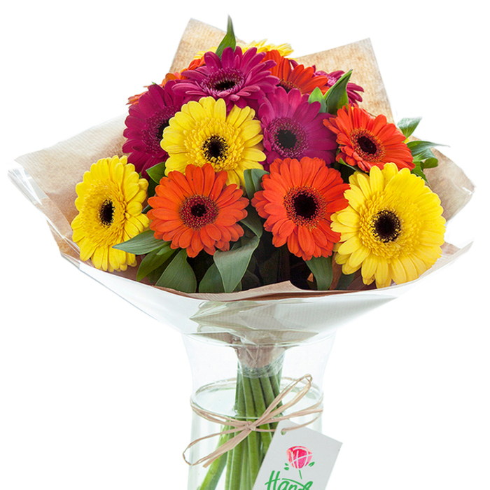 A lavish arrangement of Gerbera daisies sits proudly in a clear glass vase, reflecting the joyful spirit and garden heritage of St Mary Cray. The bouquet features a carefully balanced mix of large, sun-bright yellow, tangerine orange, and rich magenta flowers, each defined by a dark center that accentuates the brilliance of the petals. Interlaced greenery offers a fresh, natural contrast, reminiscent of the landscapes along the River Cray and the inviting greenery found in nearby parks. The bouquet is expertly wrapped in ribbed, eco-friendly kraft paper-softly textured and folded to create cozy, rustic layers-and is further shielded by a crisp swathe of clear cellophane, which adds an elegant, modern touch while helping retain the flowers' vibrant freshness. The vase's transparency reveals the stems immersed in cool, clear water, kept neatly in place by a decorative loop of twine and a small, understated white gift tag with a painterly red rose. Sunlight highlights the cheerful palette and detailed arrangement, making every daisy glow. This joyful bouquet, capturing both artistry and local flavour, is ideal for gifting on birthdays, expressing gratitude, or celebrating new beginnings near Kent Road, and stands as a testament to the thoughtful service of Flower Delivery St Mary Cray.