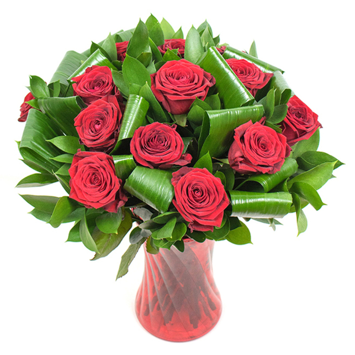 A meticulously crafted, rounded bouquet of roughly a dozen deep crimson roses is showcased here, each flower opened to an opulent, velvety bloom with petals layered in a tight, spiralled formation. The roses' intense red is made more luminous by soft, consistent lighting that reveals the subtle gradients and fine veining of each petal. Surrounding and interspersing the blooms is an abundant selection of dark green foliage: flat, glossy leaves-suggestive of Ruscus or Salal-form a dense, verdant backdrop, while larger, bright green leaves have been artfully rolled and folded into elegant spirals and arcs. These sculpted leaves act as both visual punctuation and structural support, cradling the rose heads and adding a modern, architectural quality to the overall design. The bouquet is held in a tall, slender red glass vase with a faintly ribbed or twisted texture that creates vertical lines of light and shadow, complementing the roses' passionate hues and adding a refined, tactile presence. Against a pure white background, the composition appears bold and uncluttered; the colors pop and the textures-velvety petals, glossy leaves, and smooth glass-are distinctly legible. As a florist familiar with the local neighbourhood, I picture this arrangement gracing a table in St Mary Cray High Street's quieter bistros or arriving as a romantic gift to a home near St Paul's Cray, offering a timeless expression of love and celebration while showcasing contemporary floral technique and careful material choice.