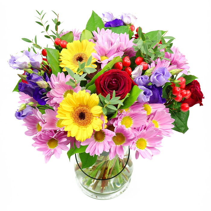Standing tall in a simple clear glass vase, this mixed bouquet is photographed against a pure white background, highlighting the interplay of colours and shapes within the arrangement. At its heart, richly shaded red roses with velvety, spiralling petals create a focal point of classic romance and depth. Framing them are two bright yellow gerbera daisies, their dark central disks surrounded by rings of vivid golden petals that seem to radiate warmth, like captured sunlight over the rooftops of St Mary Cray. Encircling this central cluster, soft pink and lavender daisies or chrysanthemums mass together in generous groups, their numerous slender petals fanning out around tiny yellow centres, producing a fluffy, textured halo that gives the bouquet fullness and a gentle, comforting feel. Interspersed among these are elegant purple and lilac lisianthus, their bell-shaped blossoms and slightly ruffled edges introducing cooler tones and a sense of layered height, almost like small, graceful brushstrokes within the design. Here and there, glossy red hypericum berries peep out on thin stems, providing bright, rounded accents that mirror the rose tones and offer a contemporary twist. The arrangement is cradled by a wealth of greenery-from broad, deep-green leaves that frame the base to finer, paler sprigs that add lightness and a garden-fresh character similar to the greenery found around local parks and riverside paths in St Mary Cray. Through the clear glass vase, neatly trimmed stems are visible in fresh water, showing the careful preparation behind the display. The bouquet feels ideal for celebrating milestones, sending a heartfelt thank-you, or simply bringing a burst of uplifting colour and soft fragrance into everyday life in St Mary Cray.